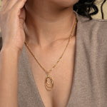 Load image into Gallery viewer,  A close-up of a model wearing a modern gold statement necklace from Zewory Jewellery. The elegant figaro chain leads to a triple oval hoop pendant with a sparkling crystal accent, showcased beautifully against her neutral-coloured top.
