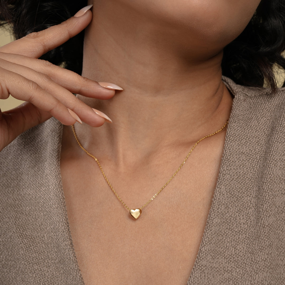 A close-up of a model wearing a delicate gold heart necklace from Zewory Jewellery. The minimalist, polished heart pendant rests elegantly in the hollow of her throat, showcasing a timeless and romantic accessory perfect for everyday wear.
