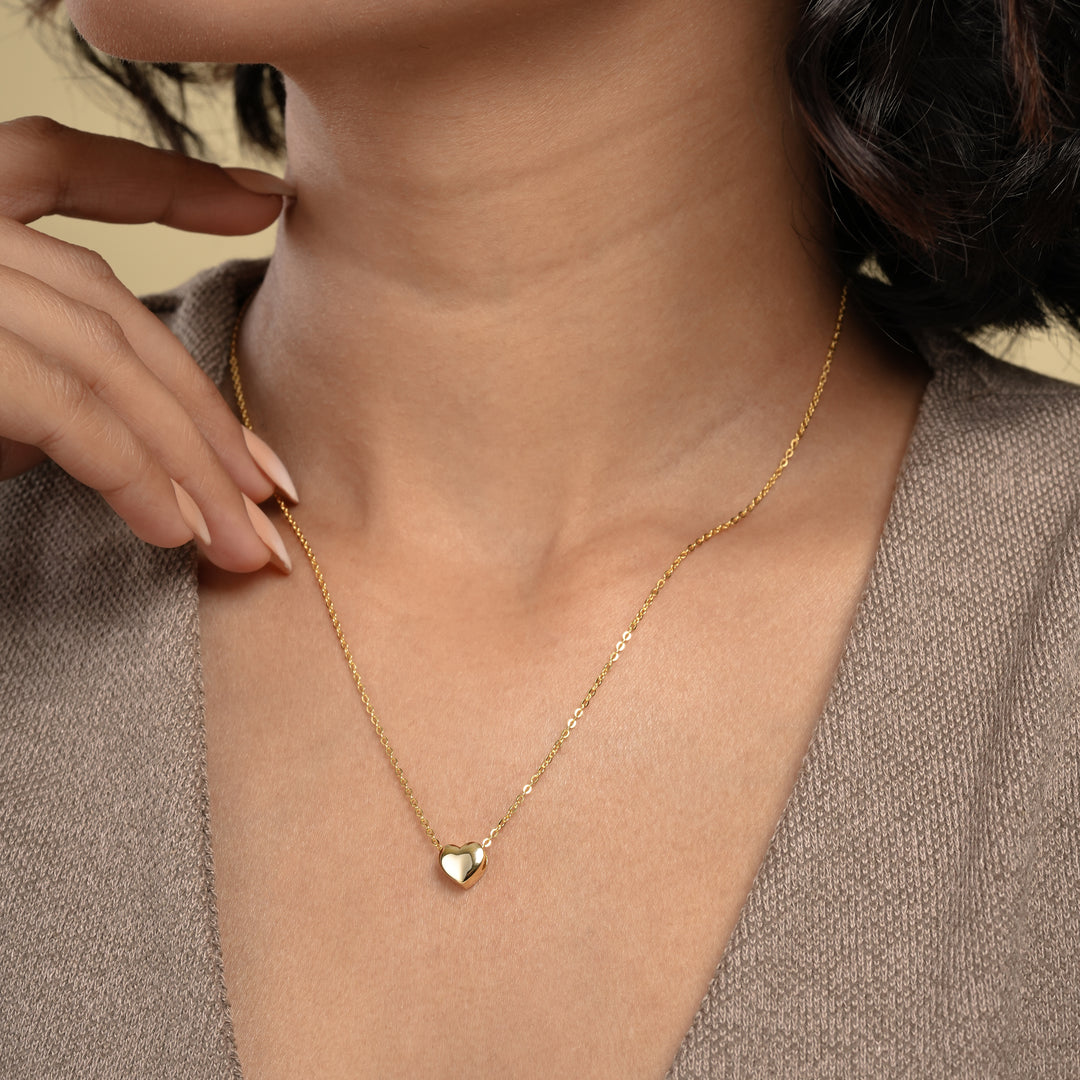 A close-up of a model wearing a delicate gold heart necklace from Zewory Jewellery. The minimalist, polished heart pendant rests elegantly in the hollow of her throat, showcasing a timeless and romantic accessory perfect for everyday wear.