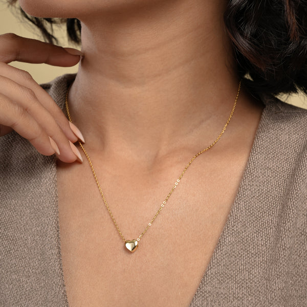 A close-up of a model wearing a delicate gold heart necklace from Zewory Jewellery. The minimalist, polished heart pendant rests elegantly in the hollow of her throat, showcasing a timeless and romantic accessory perfect for everyday wear.