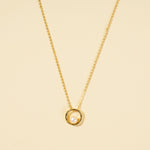 Load image into Gallery viewer, A clean, minimalist product shot of a gold and pearl necklace on a neutral cream background. The image clearly displays the modern design of a single, lustrous pearl held within a polished gold circle pendant.
