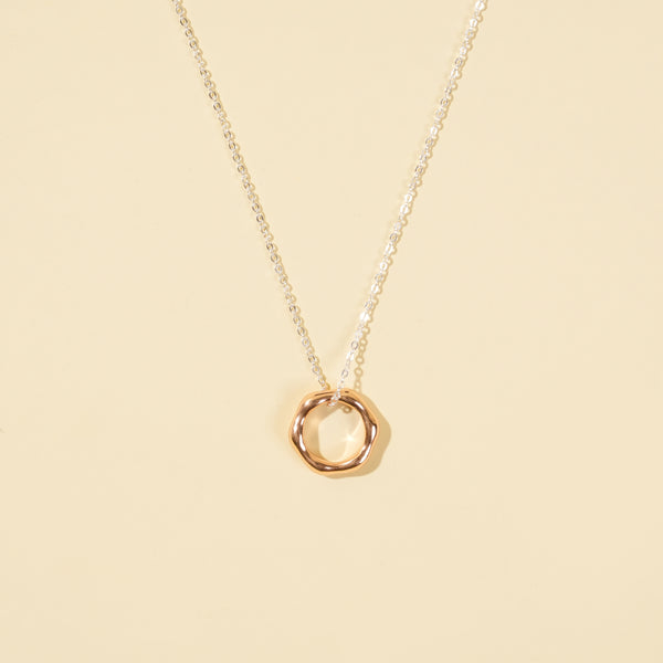 A clean, minimalist product shot of a two-tone necklace on a neutral cream background. The image clearly displays the delicate silver chain and the modern, organic-shaped rose gold open circle pendant.