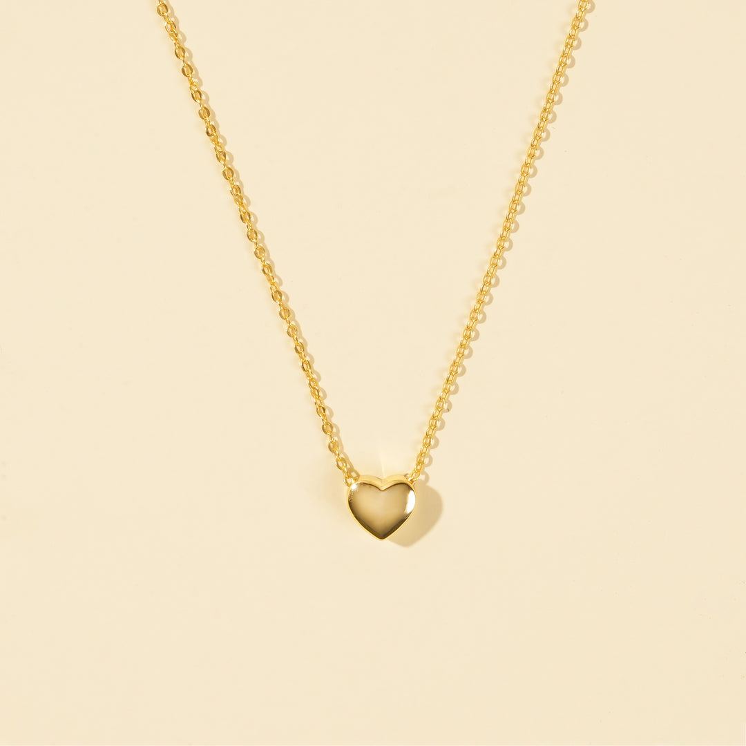 Gold heart-shaped pendant necklace on a beige background