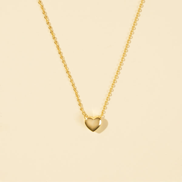 Gold heart-shaped pendant necklace on a beige background