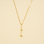 Load image into Gallery viewer, A clean, minimalist product shot of a gold Y-necklace on a neutral cream background. The image clearly displays the lariat design with a delicate drop chain accented by two polished gold spheres of graduating sizes.
