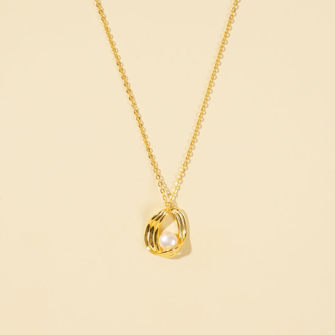 A clean, minimalist product shot of a modern gold and pearl necklace on a neutral cream background. The image clearly displays the sculptural, ribbed gold cage pendant design with a single, lustrous pearl nestled inside.