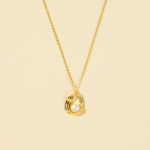 A clean, minimalist product shot of a modern gold and pearl necklace on a neutral cream background. The image clearly displays the sculptural, ribbed gold cage pendant design with a single, lustrous pearl nestled inside.
