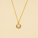 Load image into Gallery viewer, A clean, minimalist product shot of a gold celestial sun necklace on a neutral cream background. The image clearly displays the faceted sun-ray design and the open oval center lined with sparkling pavé crystals.
