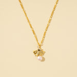 Load image into Gallery viewer,  clean product shot of a gold ginkgo leaf and pearl necklace on a neutral cream background. The image clearly displays the pleated, fan-shaped pendant with its dangling pearl, crystal accent, and decorative link chain.
