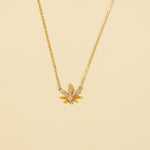 Load image into Gallery viewer, A clean, minimalist product shot of a gold cannabis leaf necklace on a neutral cream background. The image clearly displays the intricate pavé crystal detailing and the central solitaire stone on the trendy pot leaf pendant.
