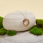 Load image into Gallery viewer, A contemporary two-tone necklace from Zewory Jewellery, displayed in a serene natural setting. The unique, molten-style rose gold circle pendant hangs from a silver chain, draped over a smooth, light-grey stone and surrounded by fresh green moss.
