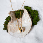 Load image into Gallery viewer, A clean, minimalist product shot of a gold honeycomb necklace on a neutral cream background. The image clearly displays the intricate barrel pendant, which features black hexagonal inlays and two bands of sparkling pavé crystals.
