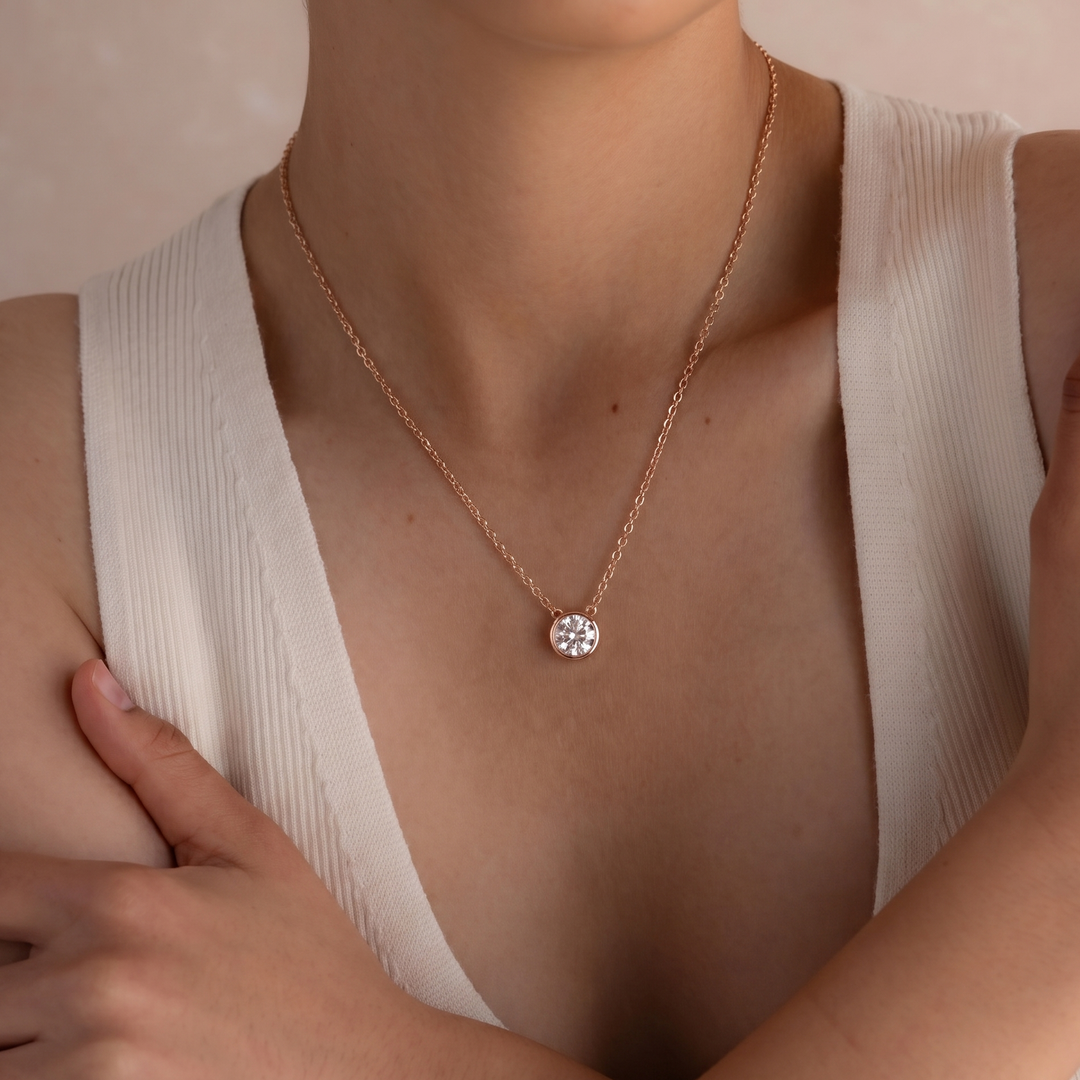 Necklace with a round pendant worn by a person in a beige top.
