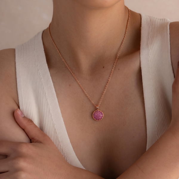 Necklace with a pink pendant worn by a person in a white top.