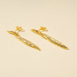 Load image into Gallery viewer, Pair of gold earrings on a beige background
