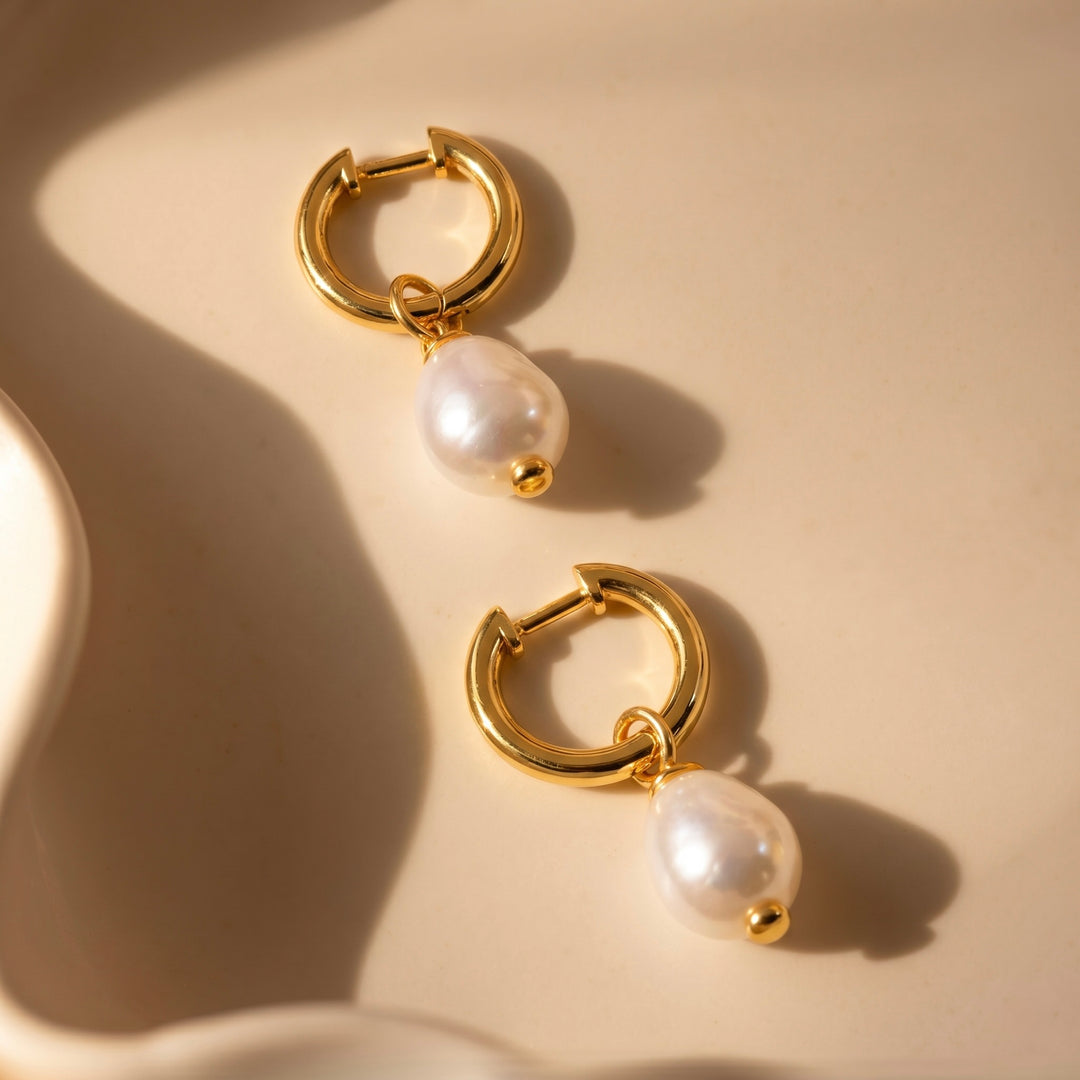 Pair of gold hoop earrings with pearl drops on a beige background