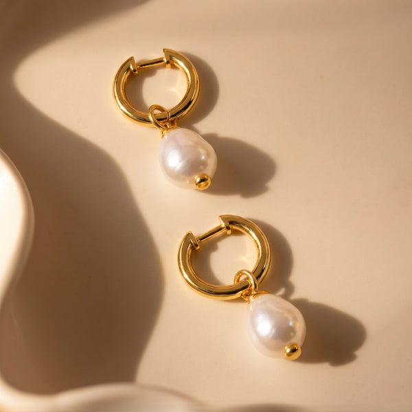 Pair of gold hoop earrings with pearl drops on a beige background