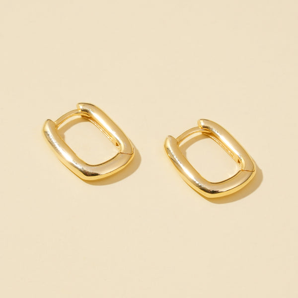 Pair of gold hoop rectangle earrings on a beige background