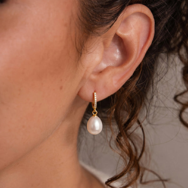 Close-up of a model wearing a gold pearl huggie hoop earring.