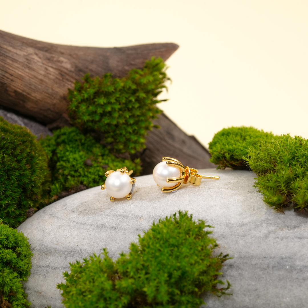 Pearl earrings with gold clasps on a stone surface surrounded by green moss.