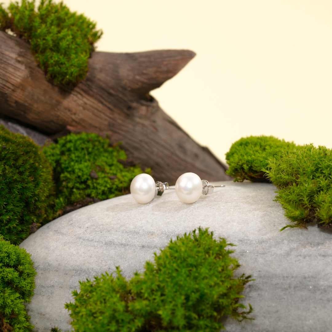 Pearl earrings on a stone with moss and wood in the background