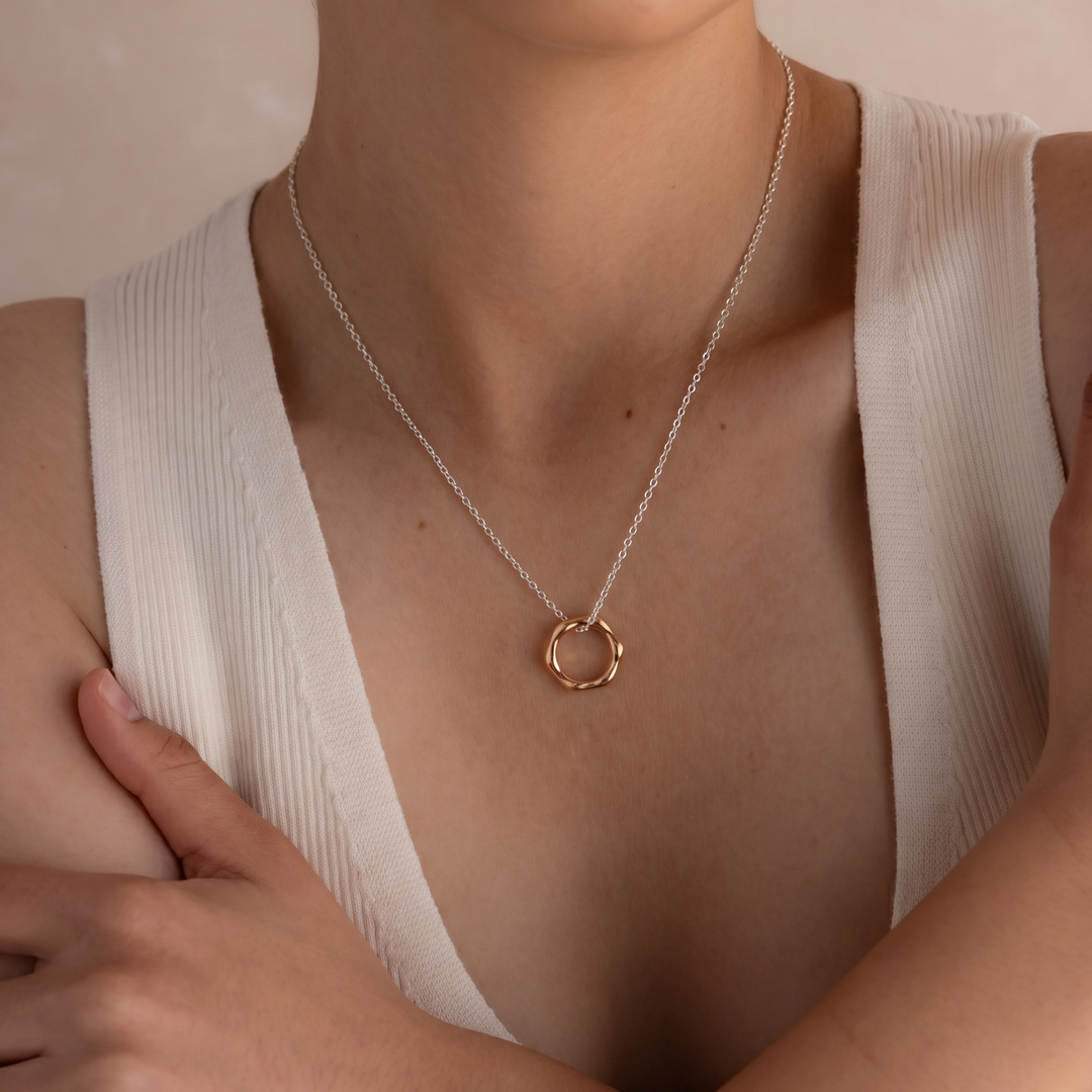 Person wearing a delicate gold necklace with a minimalistic pendant against a neutral background