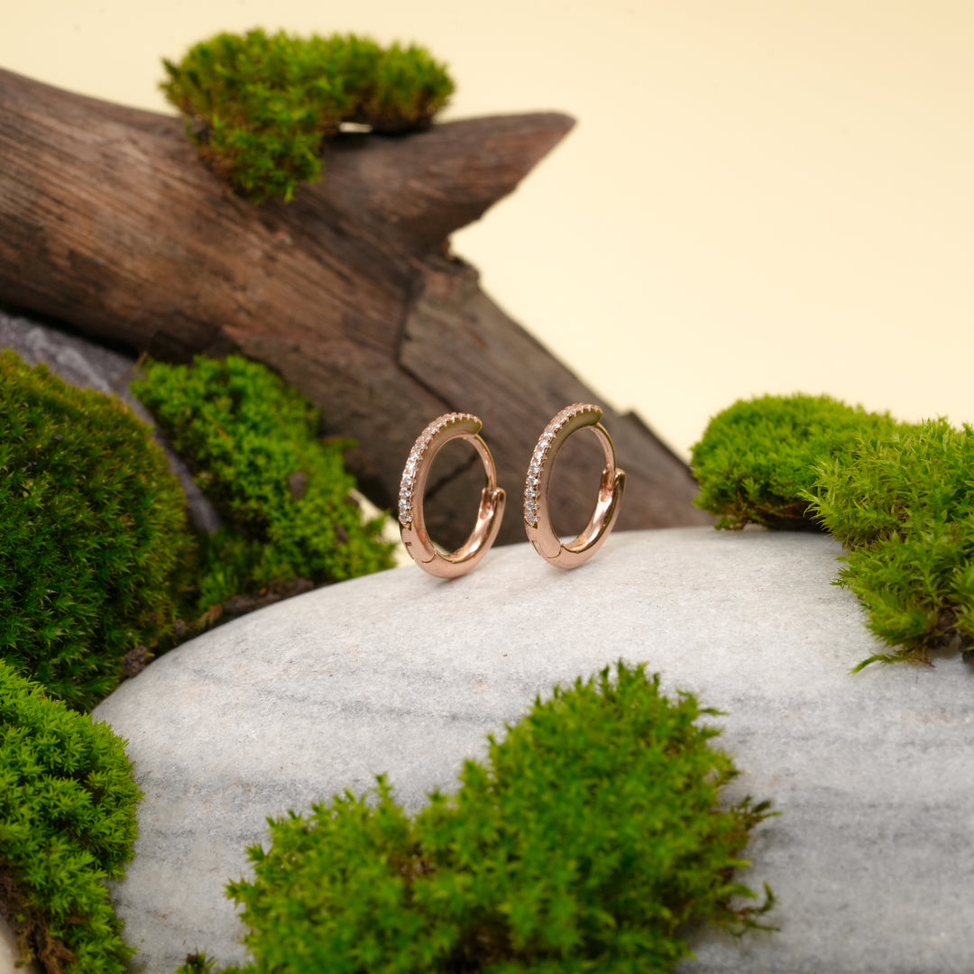 Rose gold hoop earrings on a stone with moss and wood in the background