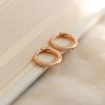 Load image into Gallery viewer, Rose gold hoop earrings with embedded stones on a light beige surface
