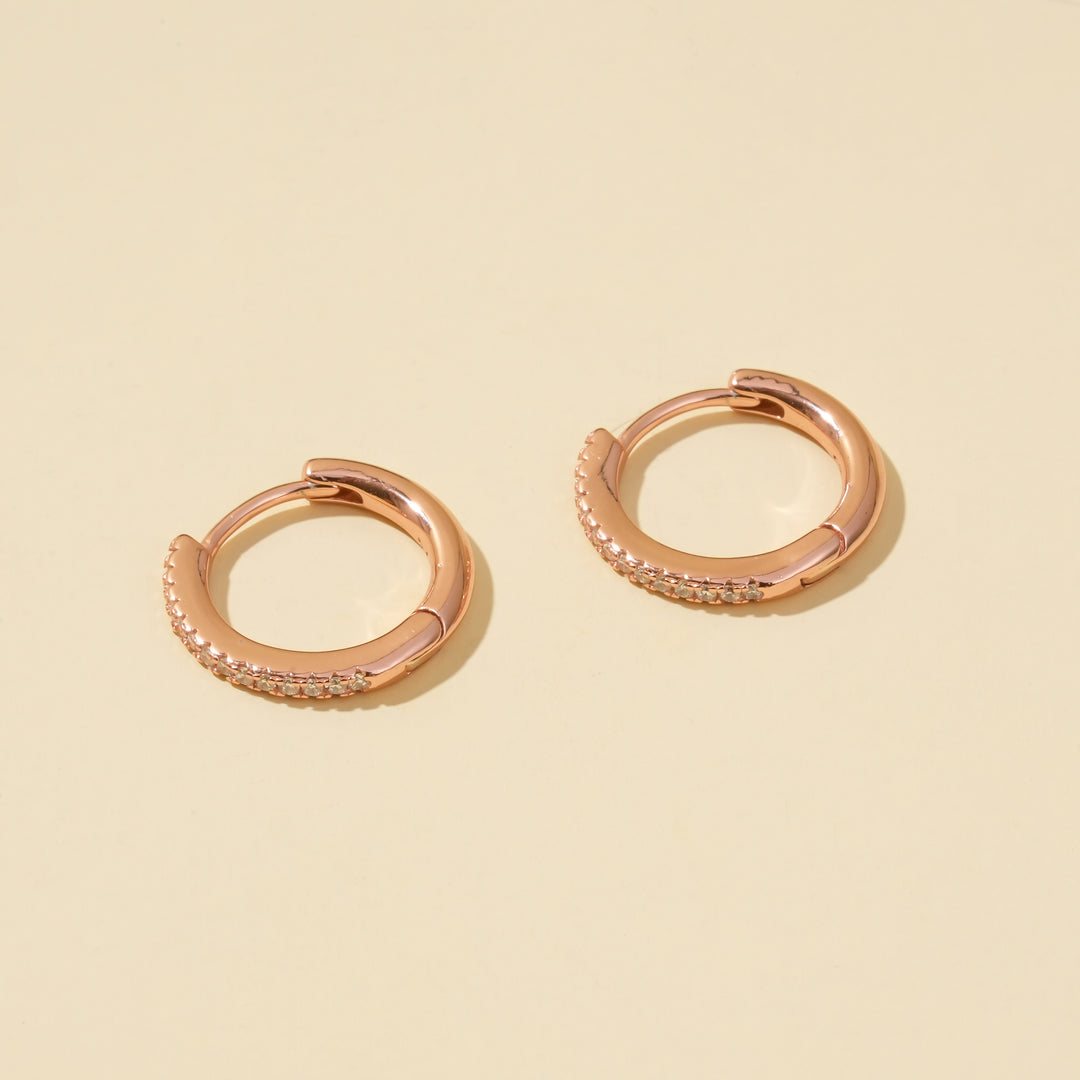 Rose gold hoop earrings with small diamonds on a beige background