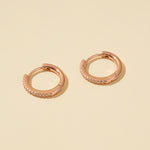 Load image into Gallery viewer, Rose gold hoop earrings with small diamonds on a beige background

