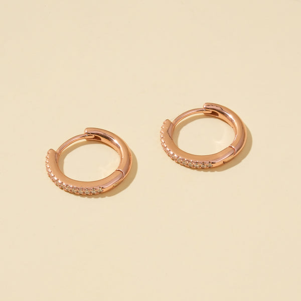 Rose gold hoop earrings with small diamonds on a beige background