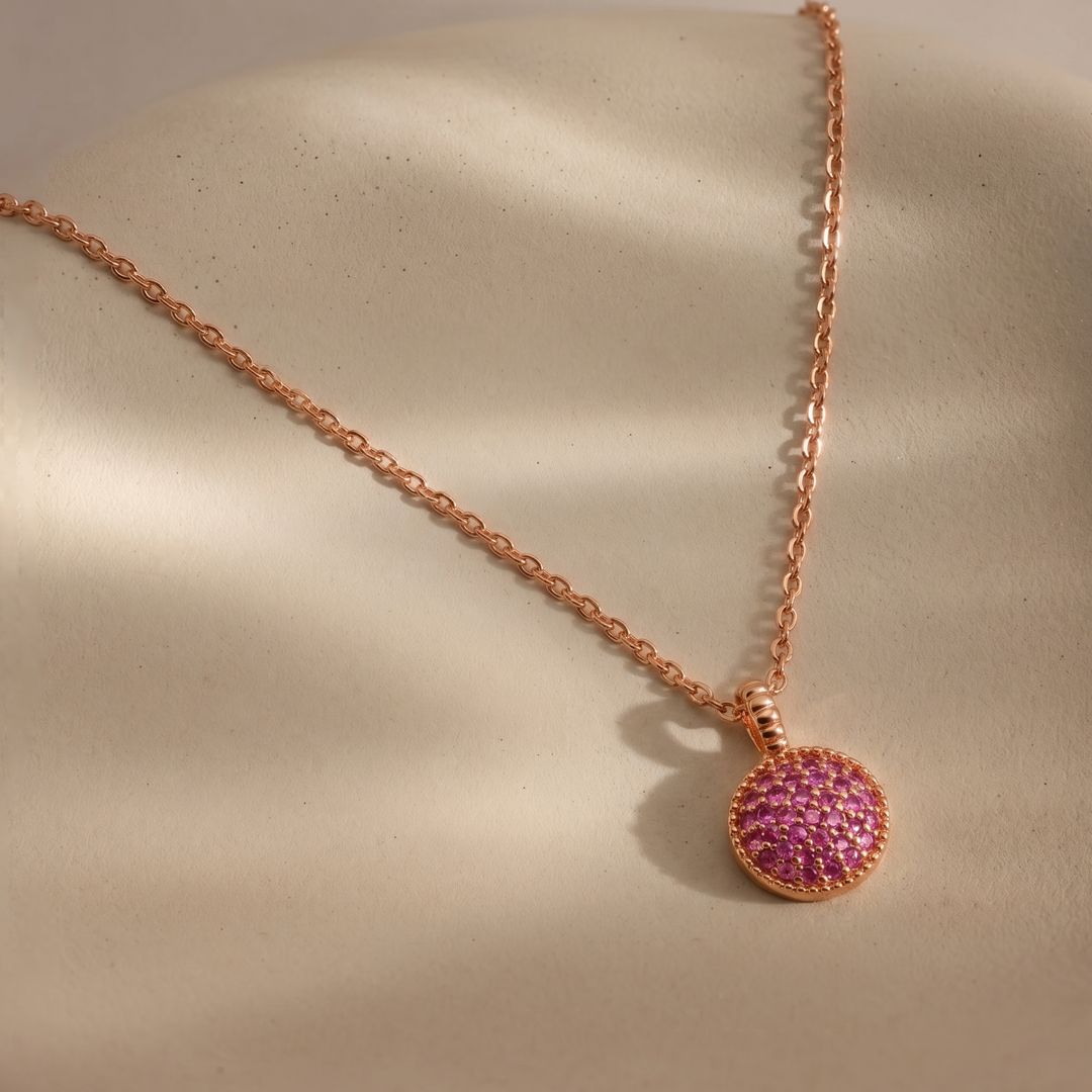 Rose gold necklace with a pink gemstone pendant on a beige surface