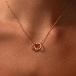 Load image into Gallery viewer, Rose gold necklace with interlocking rings on a person's neck against a warm-toned background
