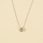 Load image into Gallery viewer, Silver necklace with a double interlocking ring pendant on a beige background
