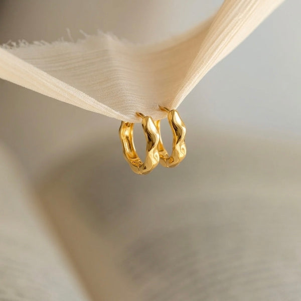 Two gold hoop earrings hanging from a wooden hook against a neutral background