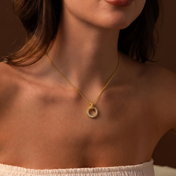 Woman wearing a gold necklace with a pearl pendant against a brown background