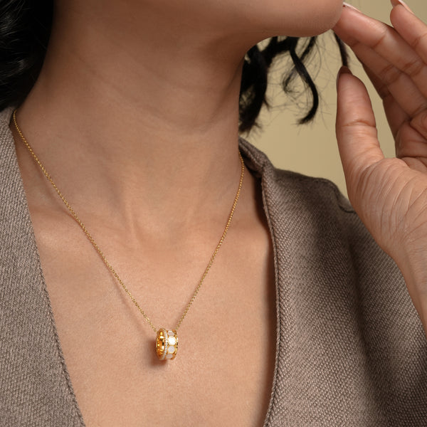 A close-up of a model wearing an elegant gold necklace from Zewory Jewellery. The unique barrel pendant, featuring a white mother-of-pearl honeycomb pattern and a sparkling pavé crystal band, is showcased against her neutral-coloured top.