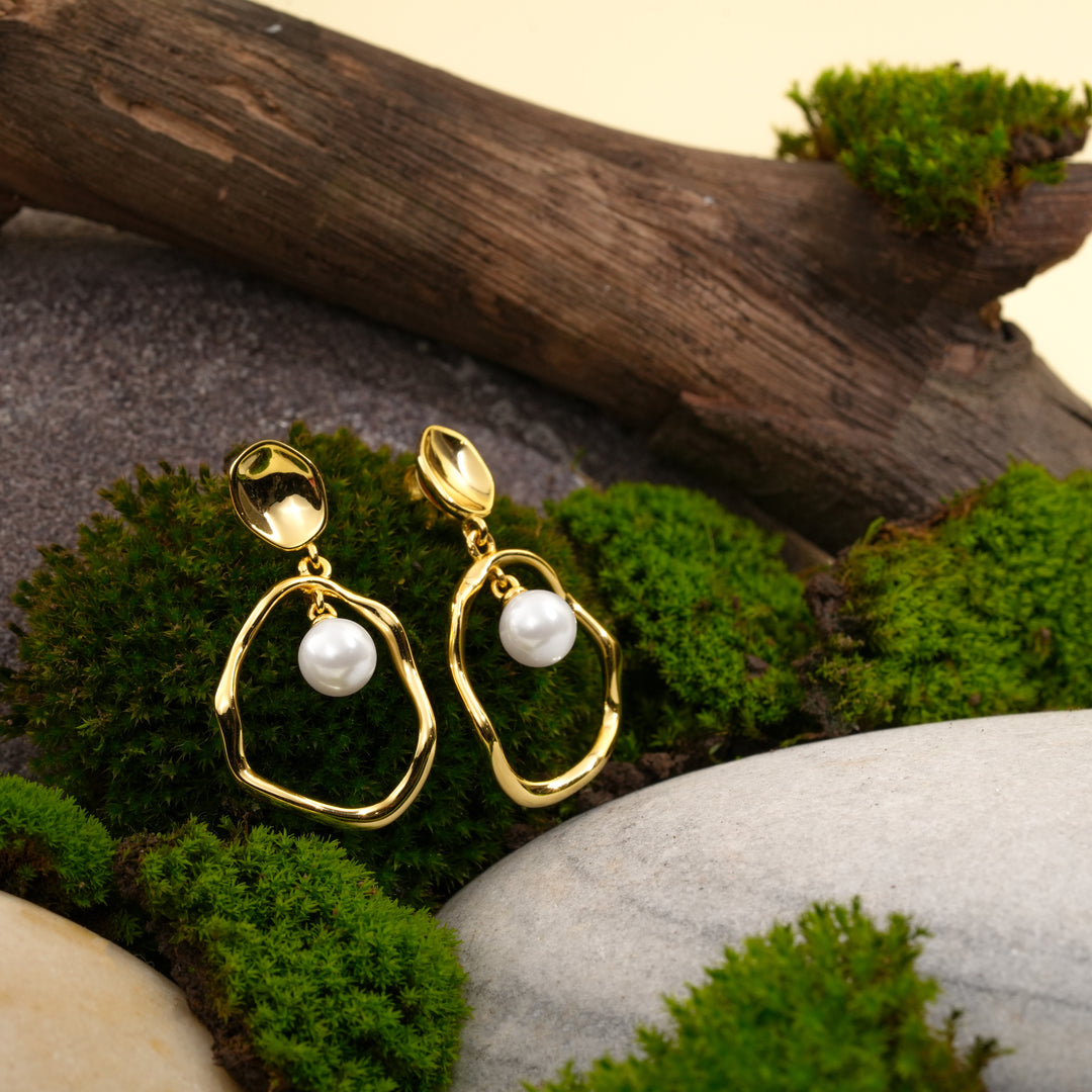 A stunning pair of organic-shaped gold and pearl statement earrings. This creative product shot from Zewory Jewellery displays the dangle earrings in a natural setting of rich green moss, stones, and weathered wood.