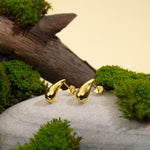 Load image into Gallery viewer, A pair of minimalist gold teardrop stud earrings from Zewory Jewellery. The modern, polished droplet design is showcased in a natural setting on a grey stone, surrounded by vibrant green moss and weathered wood.
