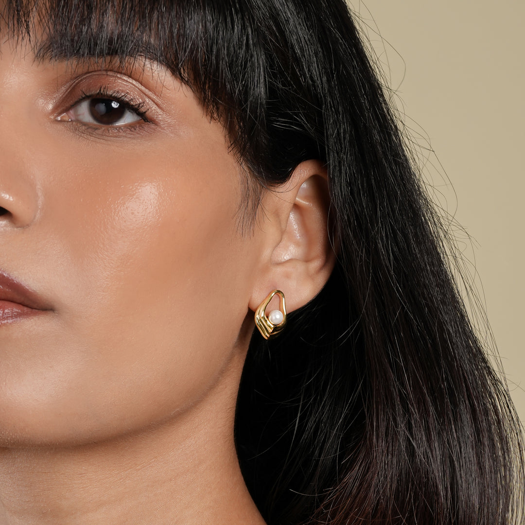 Close-up of a woman wearing gold hoop earrings with a neutral background
