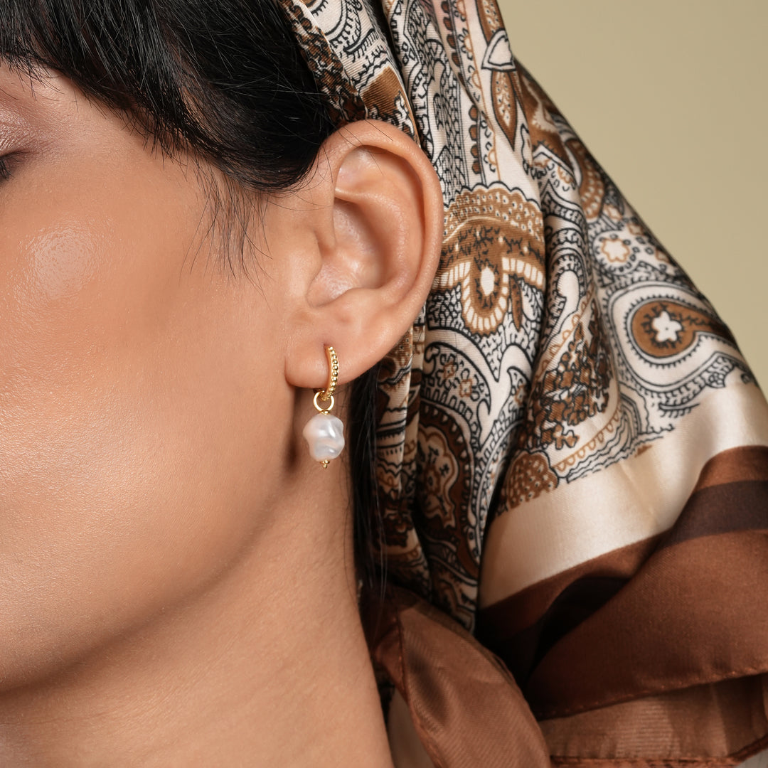 Close-up of an ear with a pearl earring, wearing a patterned brown scarf.
