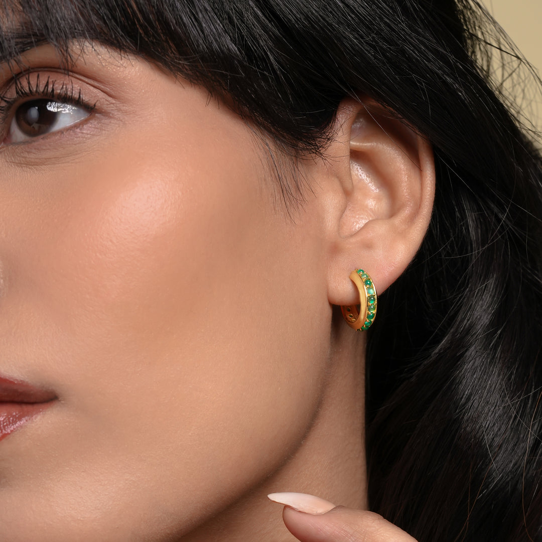 Close-up of a woman wearing gold hoop earrings with green gemstones.