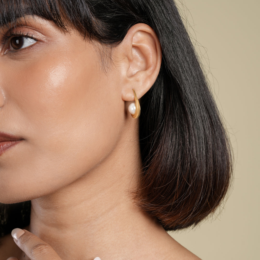 Close-up of a woman wearing a gold earring with a pearl on a beige background