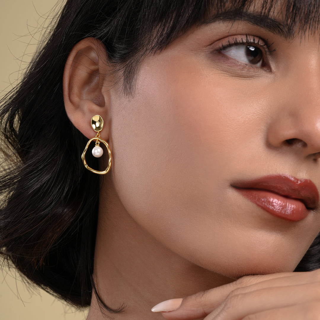 Close-up of a woman wearing a gold earring with a pearl on a beige background