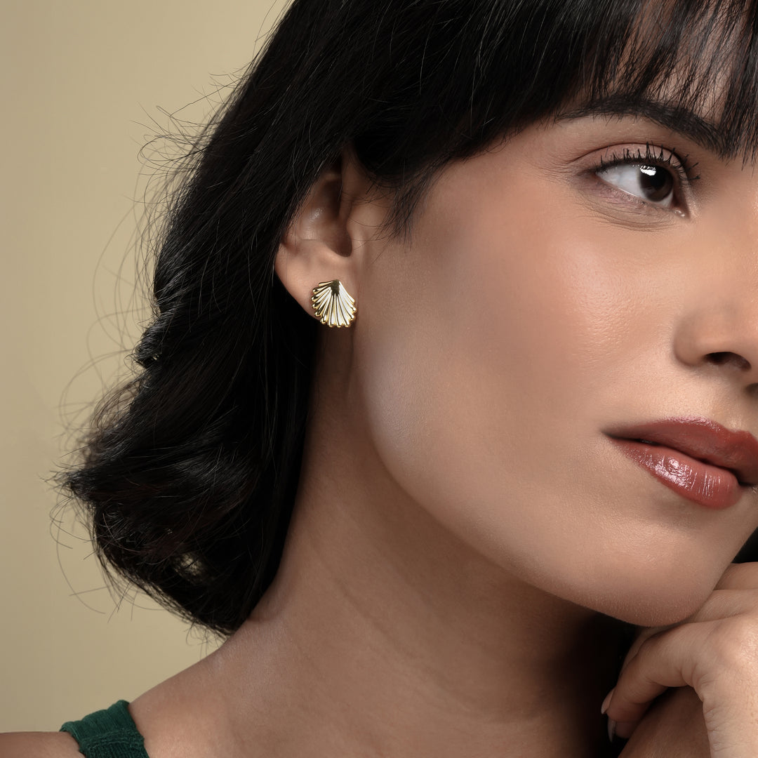 A close-up of a model wearing a delicate gold seashell stud earring from Zewory Jewellery. The detailed, ribbed scallop shell design sits elegantly on her earlobe, showcasing a chic, ocean-inspired accessory.