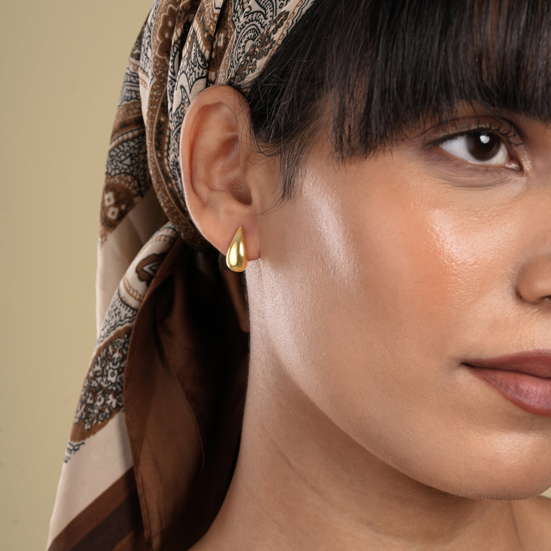 Close-up of a woman wearing a gold earring with a patterned headscarf on a beige background