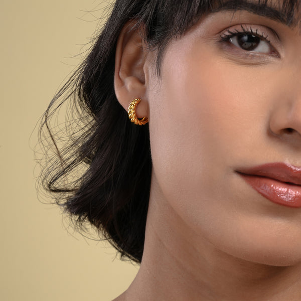 A close-up of a model wearing a chic, twisted gold hoop earring from Zewory Jewellery. The small, croissant-style hoop elegantly hugs her earlobe, showcasing a trendy and textured accessory perfect for everyday wear.