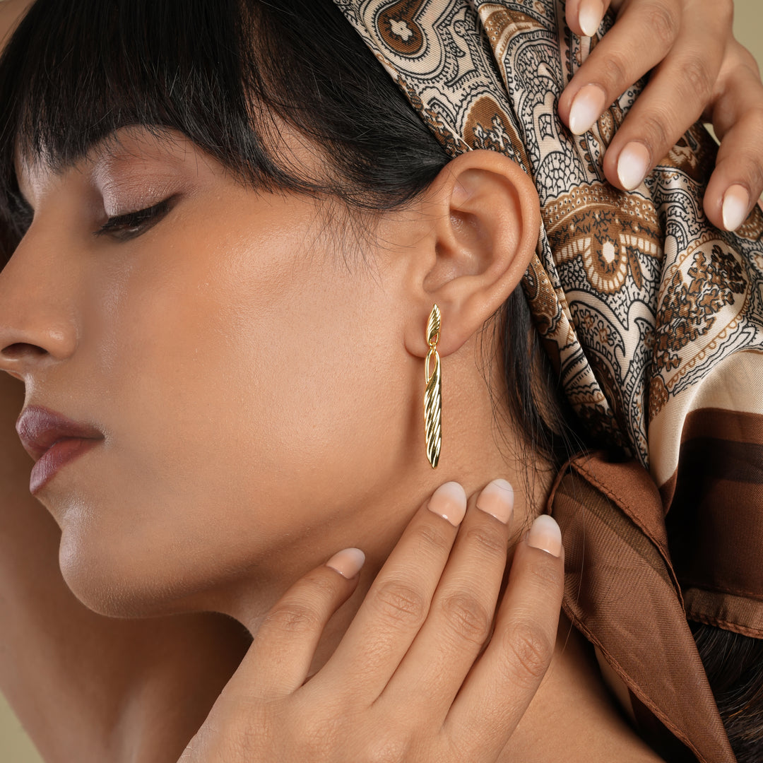 Woman wearing gold hoop earrings with a patterned headscarf and hands adjusting it.