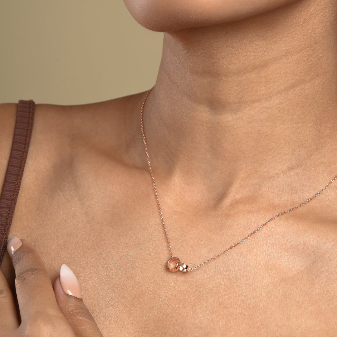 A close-up of a model wearing a delicate rose gold necklace with a symbolic interlocking rings pendant. The minimalist double-circle design sits elegantly against her skin, showcasing a timeless and meaningful piece of fashion jewellery.