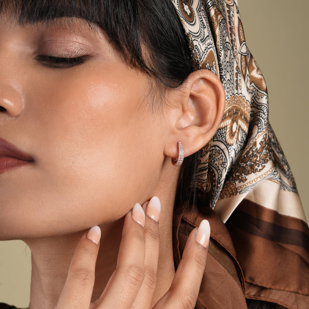 Close-up of a woman wearing a patterned headscarf and earrings with a neutral background